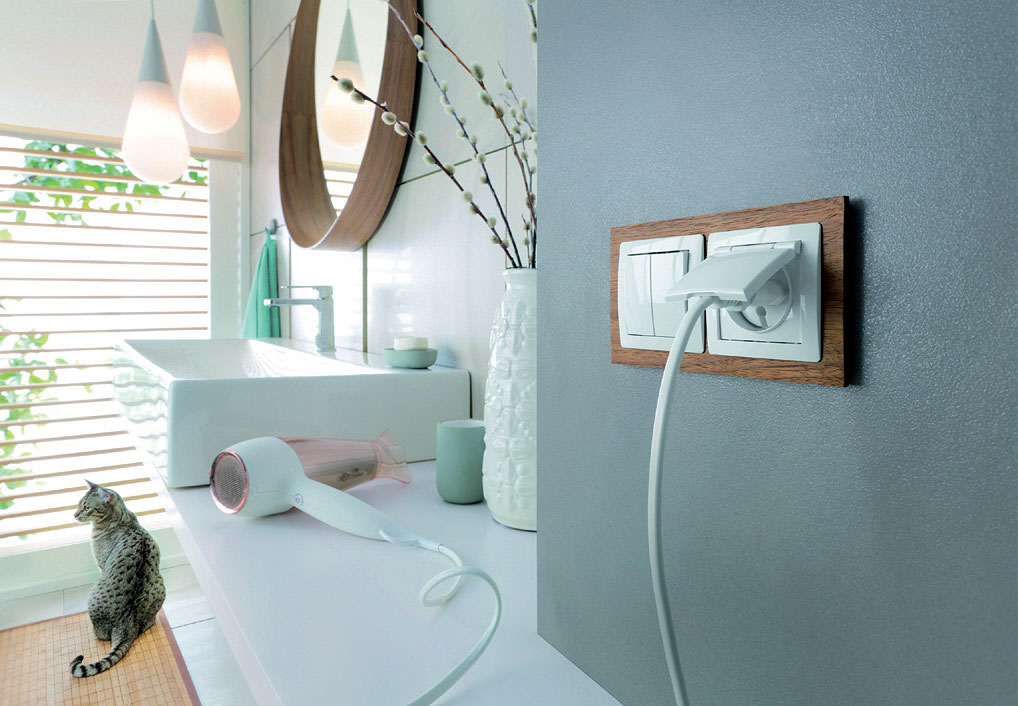 Fot. 15. Seria DECO: ramka uniwersalna z drewna podwójna, dębowa + mechanizm łącznika świecznikowego biały i mechanizm gniazda bryzgoszczelnego z uziemieniem 2P+Z biały z klapką białą. Producent: Karlik Elektrotechnik Sp. z o.o. Fot. Karlik